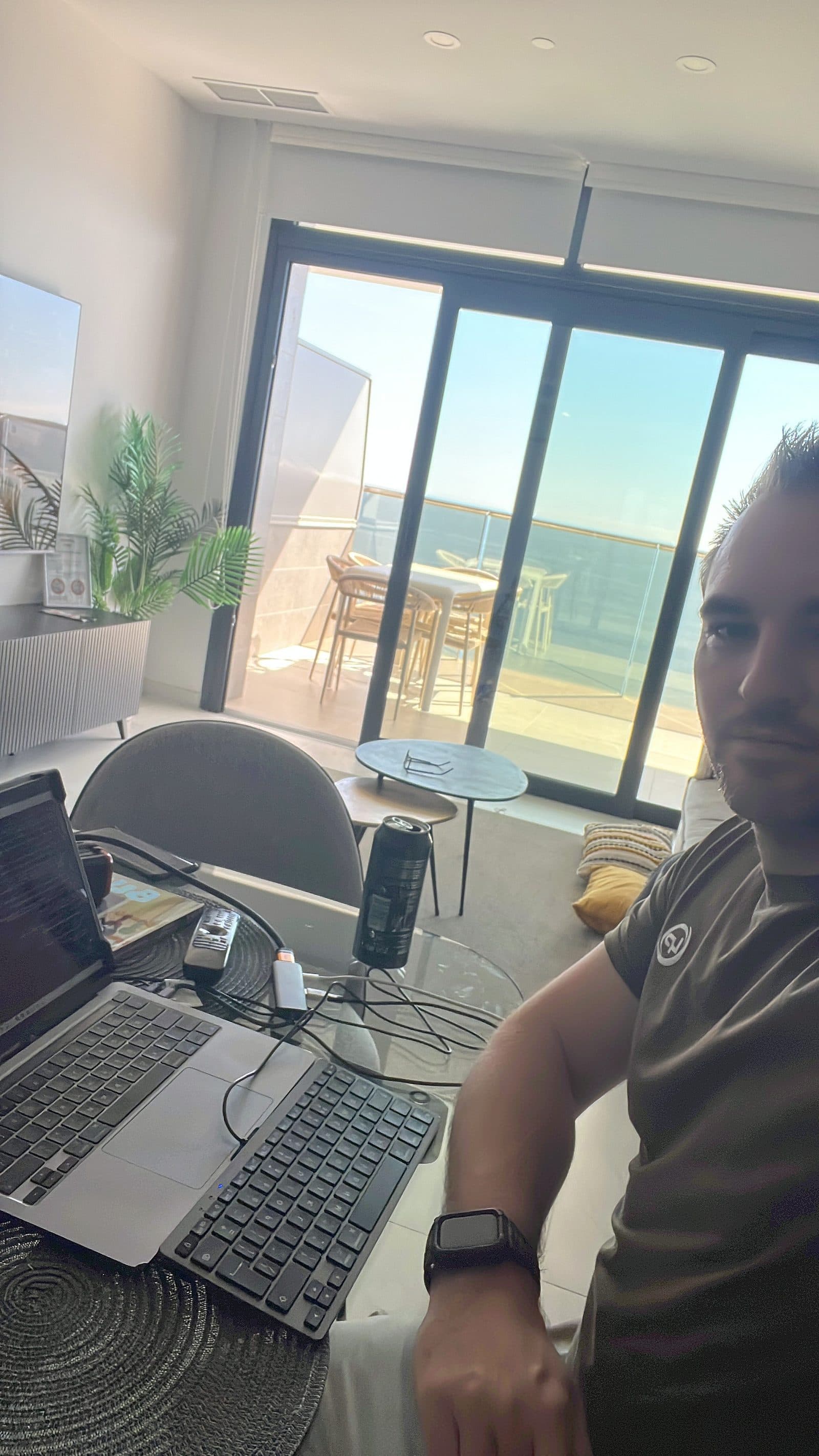 Liam working on a laptop in the Benidorm apartment with sea view through the window