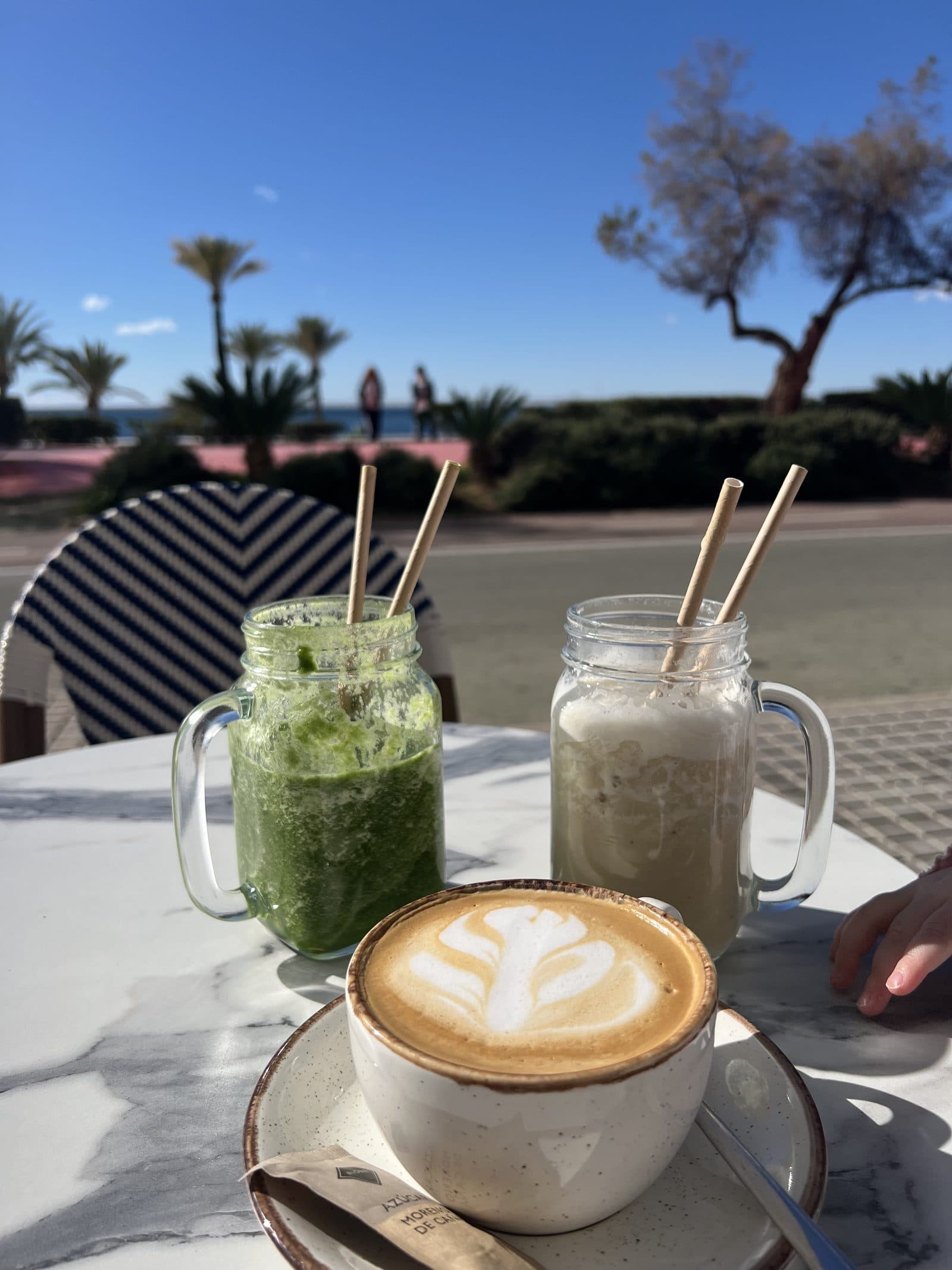 Smoothies and a latte at a beachfront cafe on Benidorm promenade with palm trees in the background