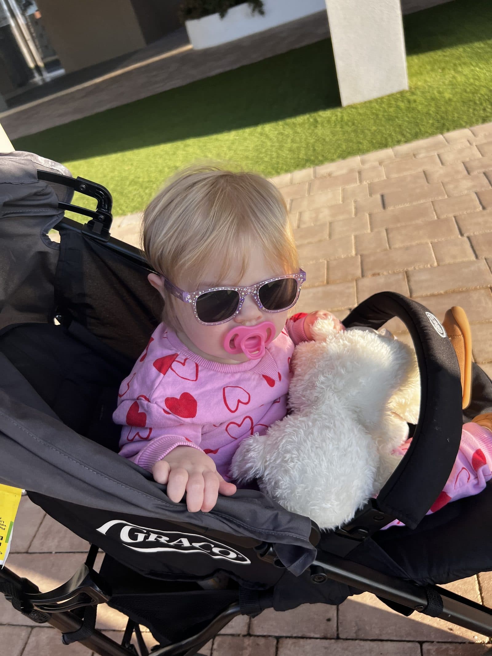 Tallulah in her pushchair wearing sunglasses and a pink heart jumper, ready for a walk along Benidorm promenade