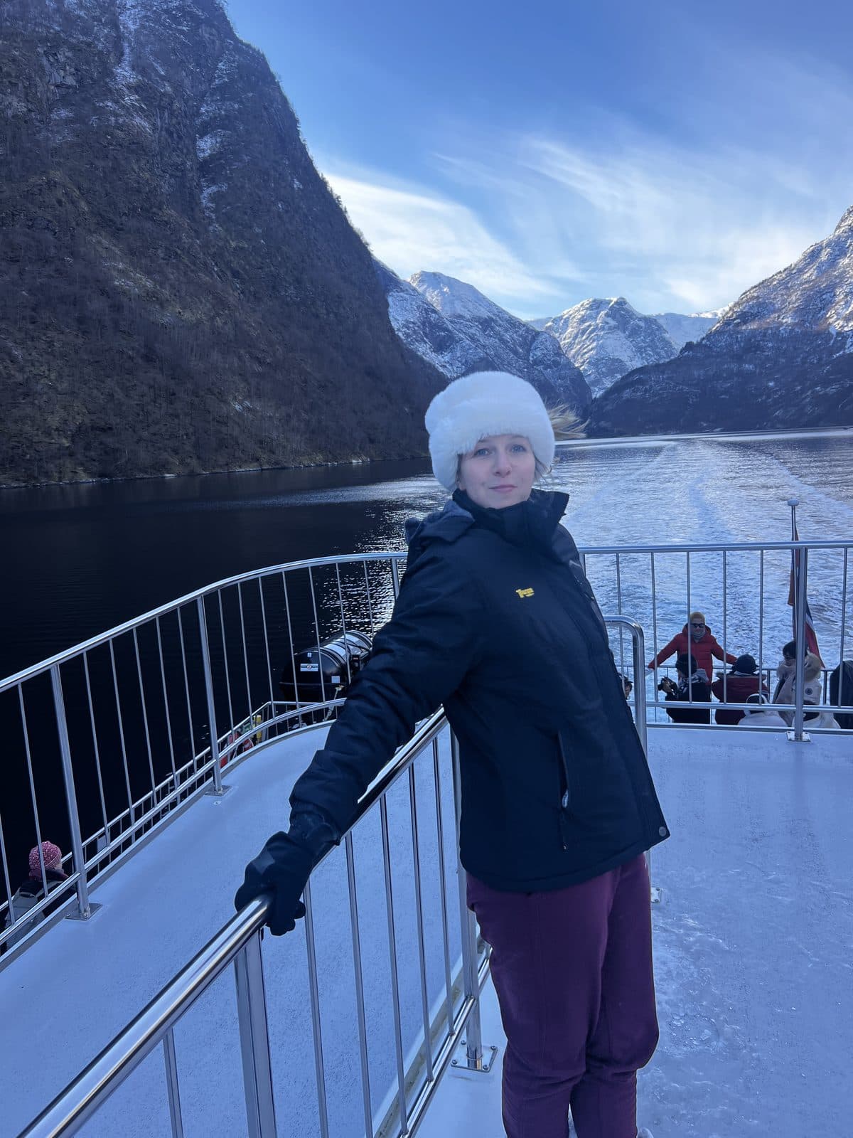 Woman on a fjord cruise boat in Norway with dramatic snow-capped mountains and fjord behind